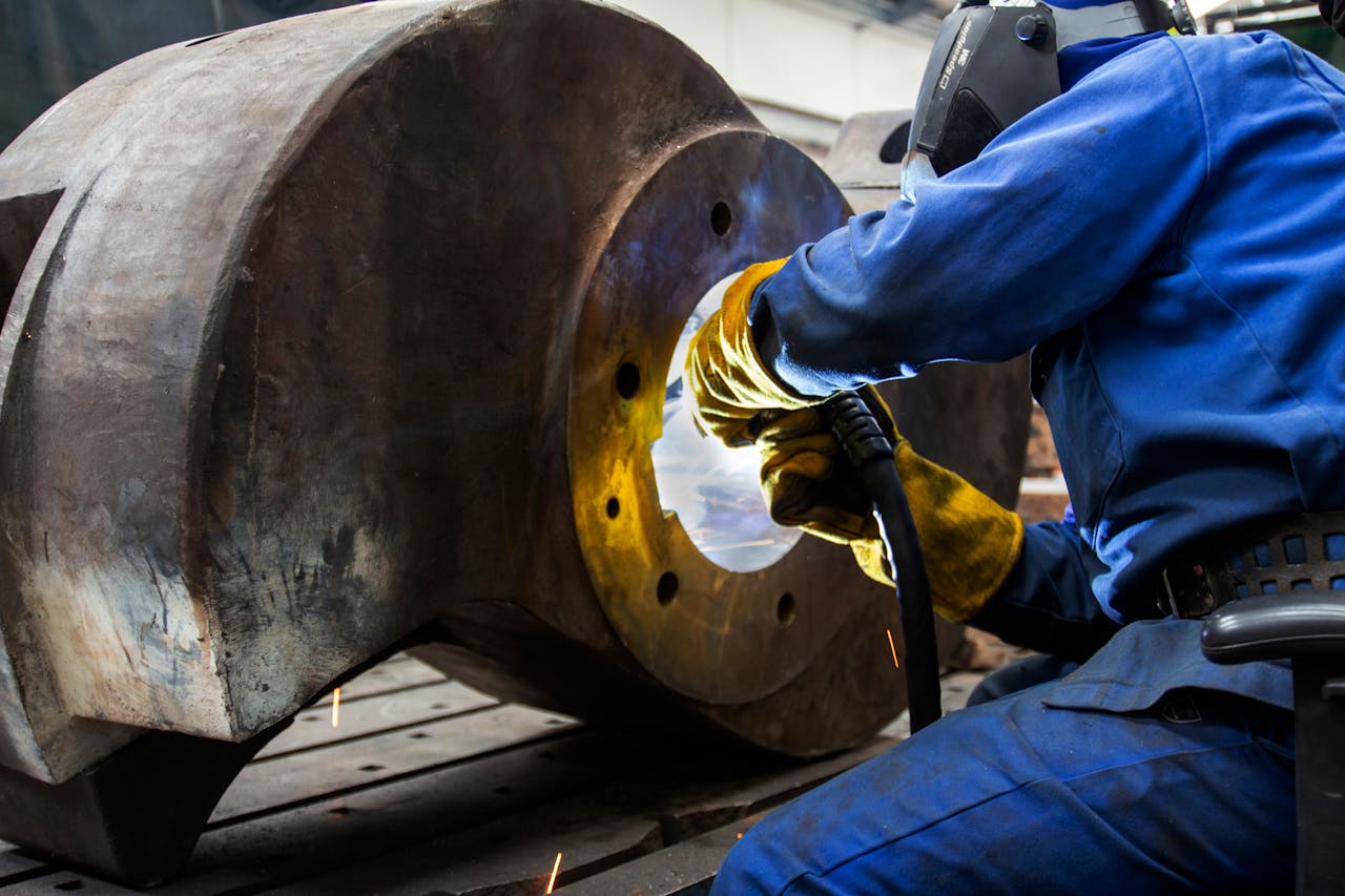 A welder wearing safety gear operates on a large metal component in an industrial setting.
